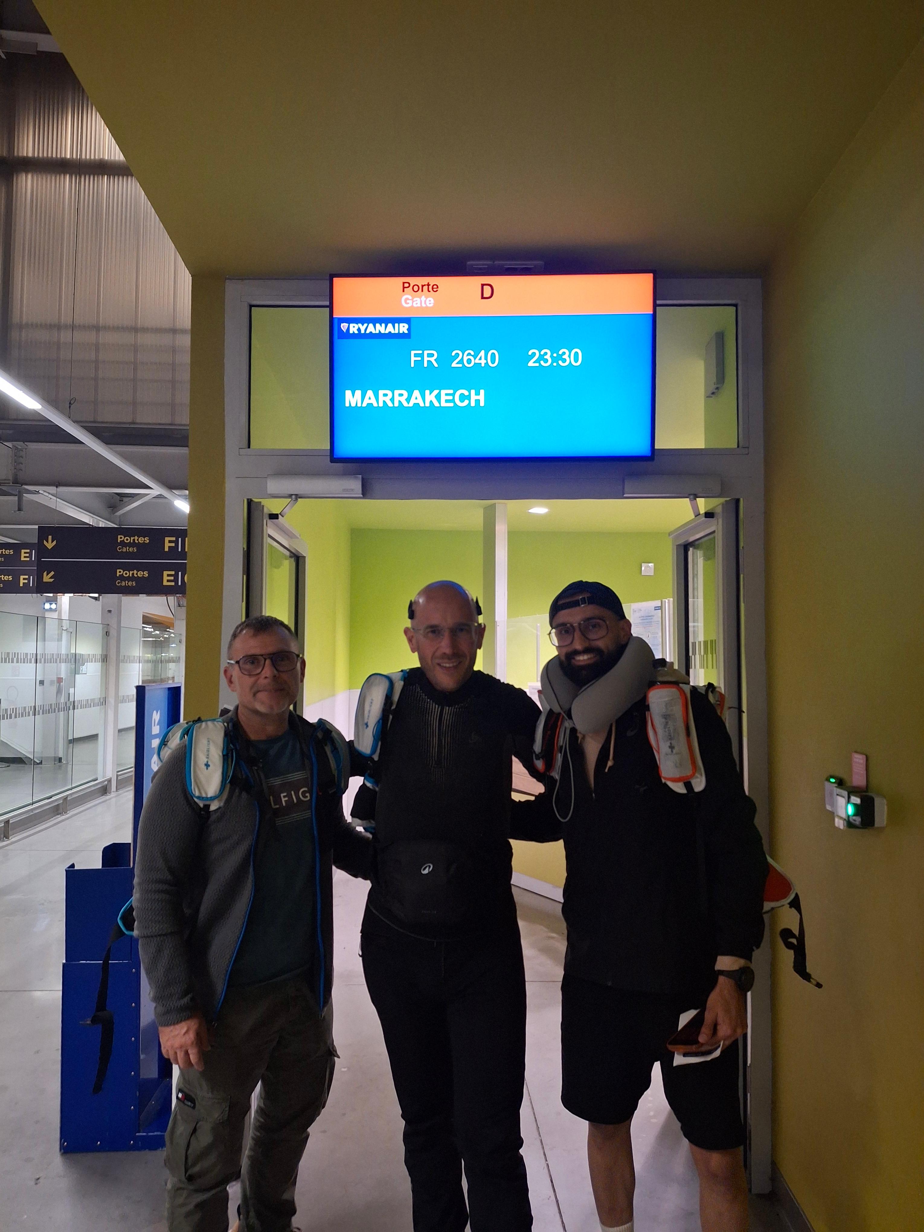 Trois hommes souriant devant la porte d'embarquement pour Marrakech
